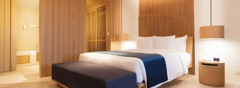 Modern luxury hotel bedroom with minimalist wooden design, white linens, and warm lighting in a 5-star hotel in Marbella.