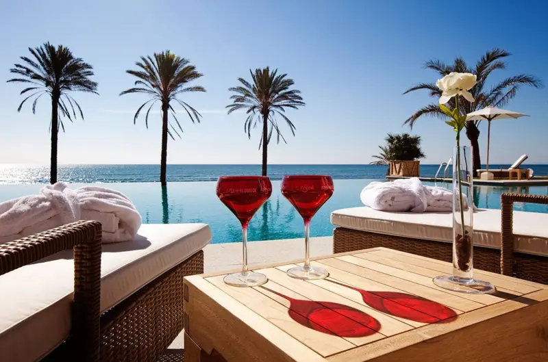 Luxury beach club with an infinity pool, palm trees, and two red cocktails.