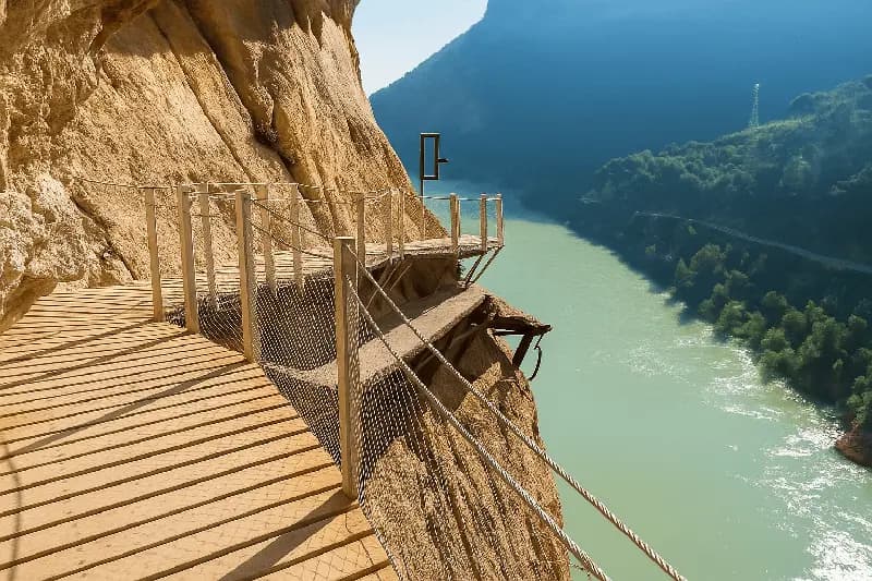 Cliffside walkway on Caminito del Rey above turquoise river with rock walls and hills in Andalusia, malaga, Spain