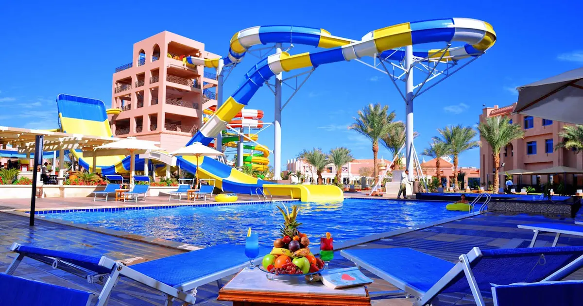 Family waterpark resort on Costa Azahar, Spain: colorful blue-yellow waterslides, pools, palm trees at family resort under sunny skies.