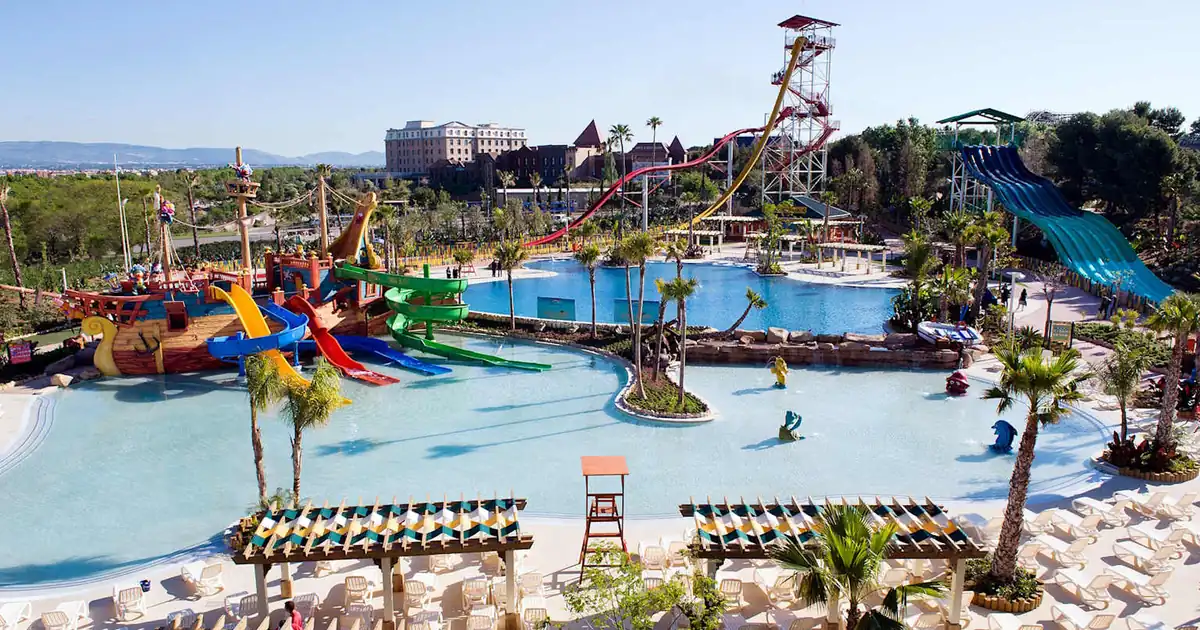 Aerial view of PortAventura World family resort on Costa Dorada, Spain: pirate ships, colorful waterslides, roller coasters, blue pools, palm trees.