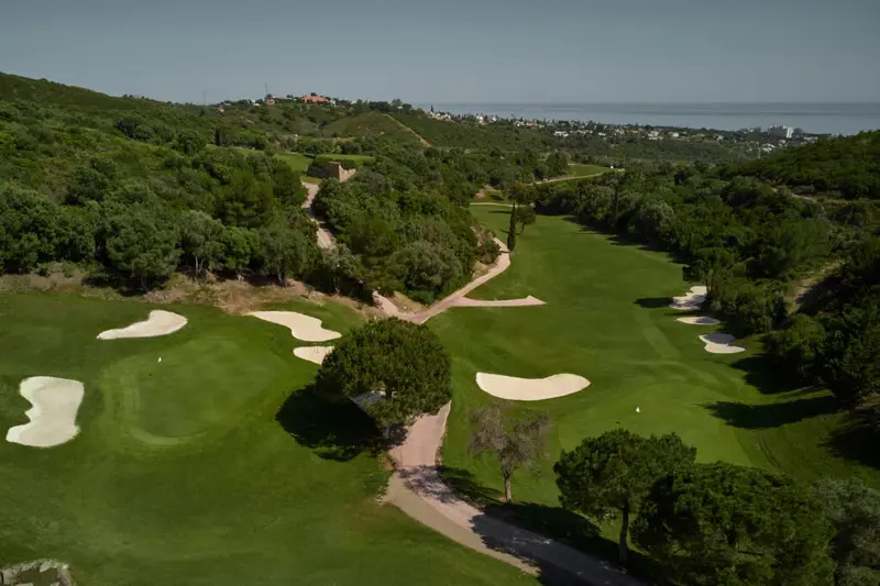 Luxury golf resort fairway overlooking the Mediterranean Sea in Costa del Sol, Spain, with palm trees and bunkers under a sunny sky.