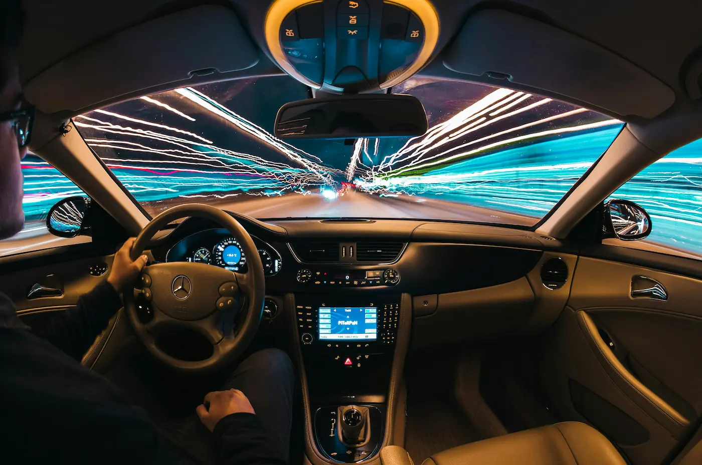 View from inside a car during a night drive; city light trails on the windshield