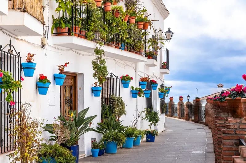 alt=Traditional white houses of Mijas Pueblo adorned with vibrant flower pots