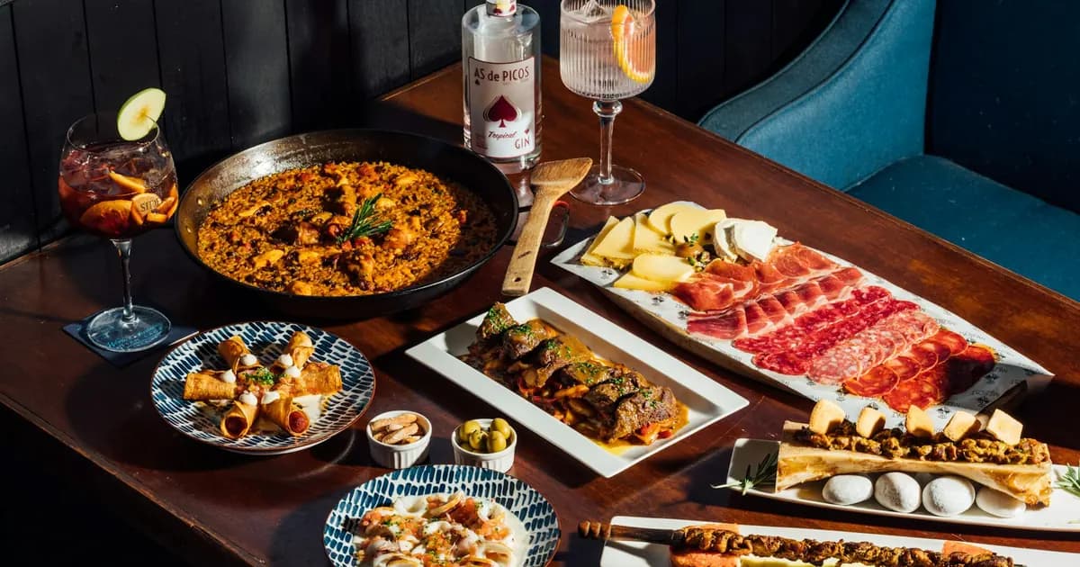 Malaga food guide: Traditional Spanish tapas spread from Malaga with paella, jamón, croquettes, skewers, and gin tonics on a table.