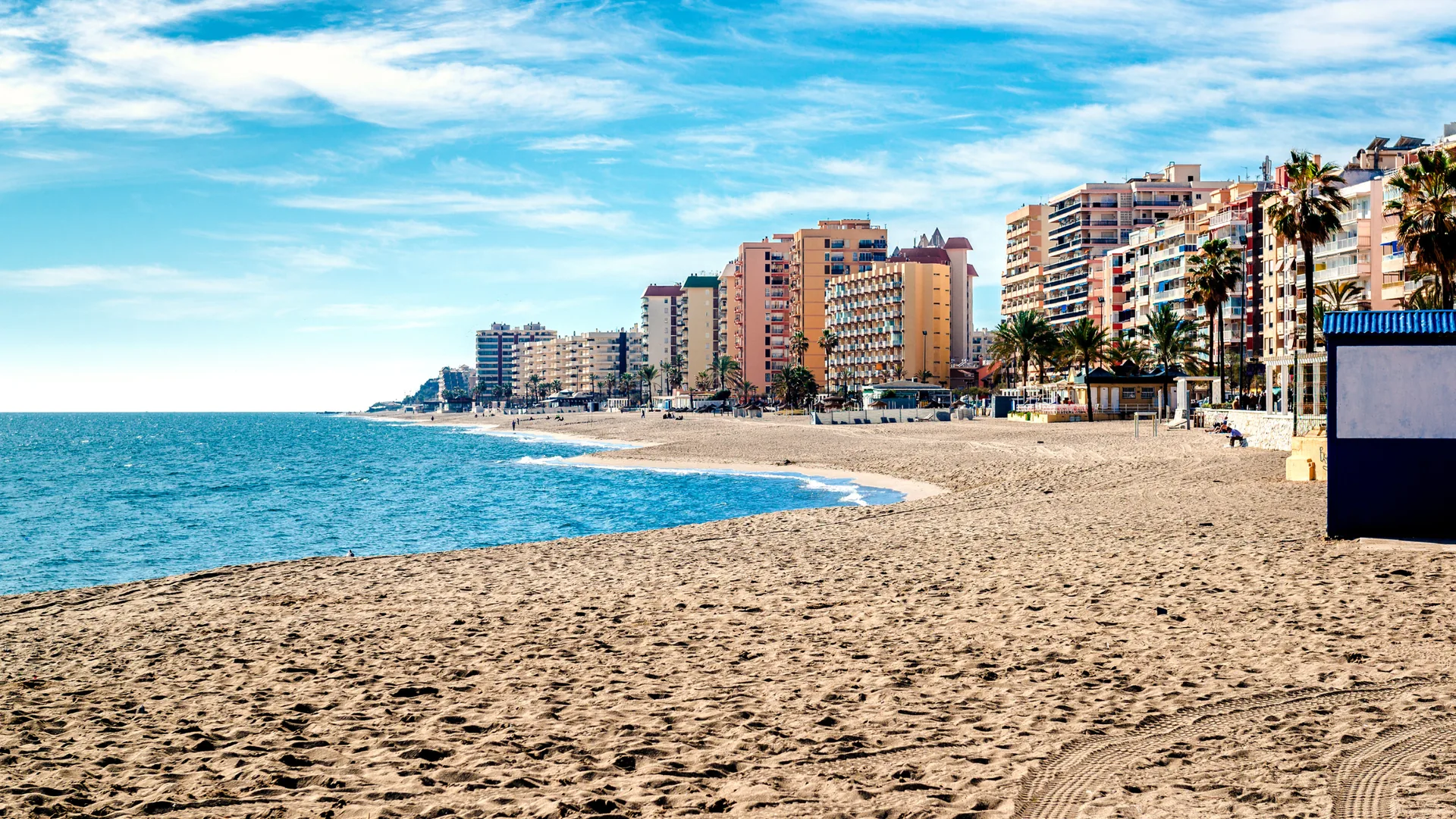 Wide sandy beach in Fuengirola with calm blue sea and a row of hotels and apartment buildings along the seafront