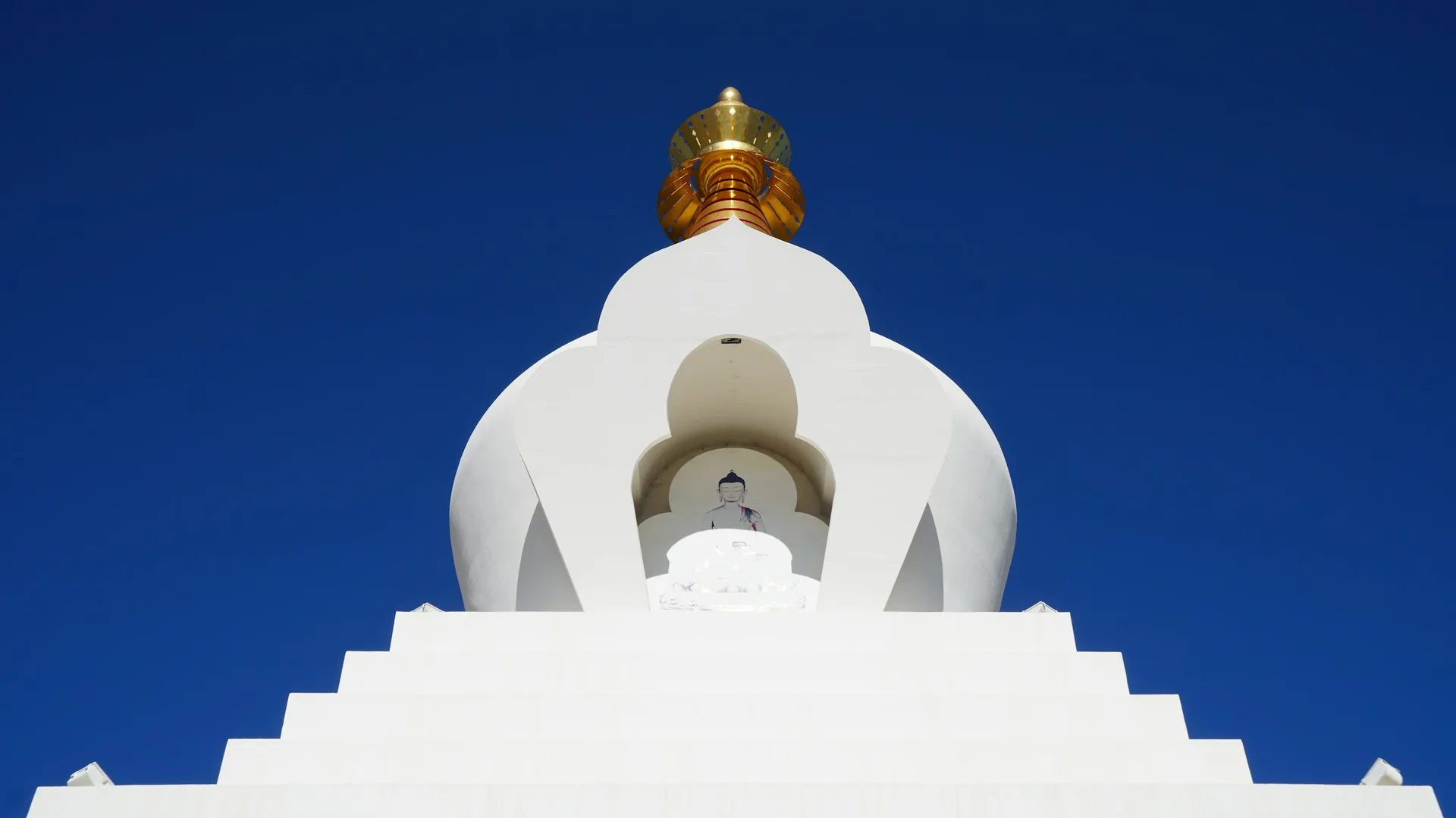 White Buddhist in Benalmádena stupa with a golden spire against a clear blue sky