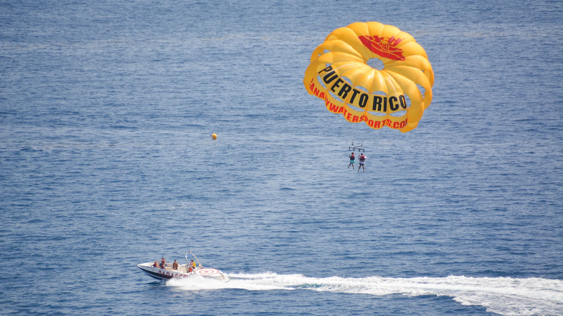 Parasailor lifted high above turquoise Mediterranean water on the Spanish coast with clear blue sky
