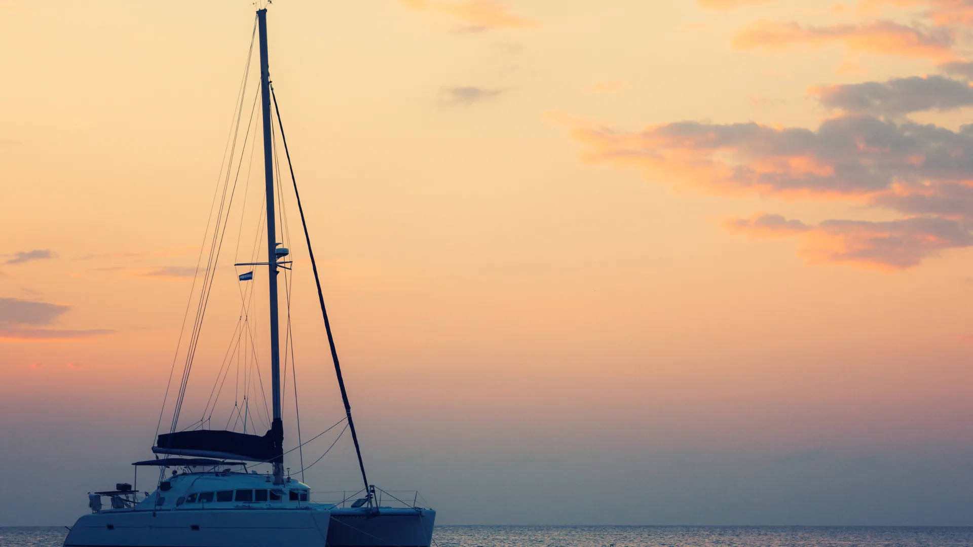 Catamaran sailboat silhouetted against a golden sunset sky on a calm sea during a boat trip from Fuengirola