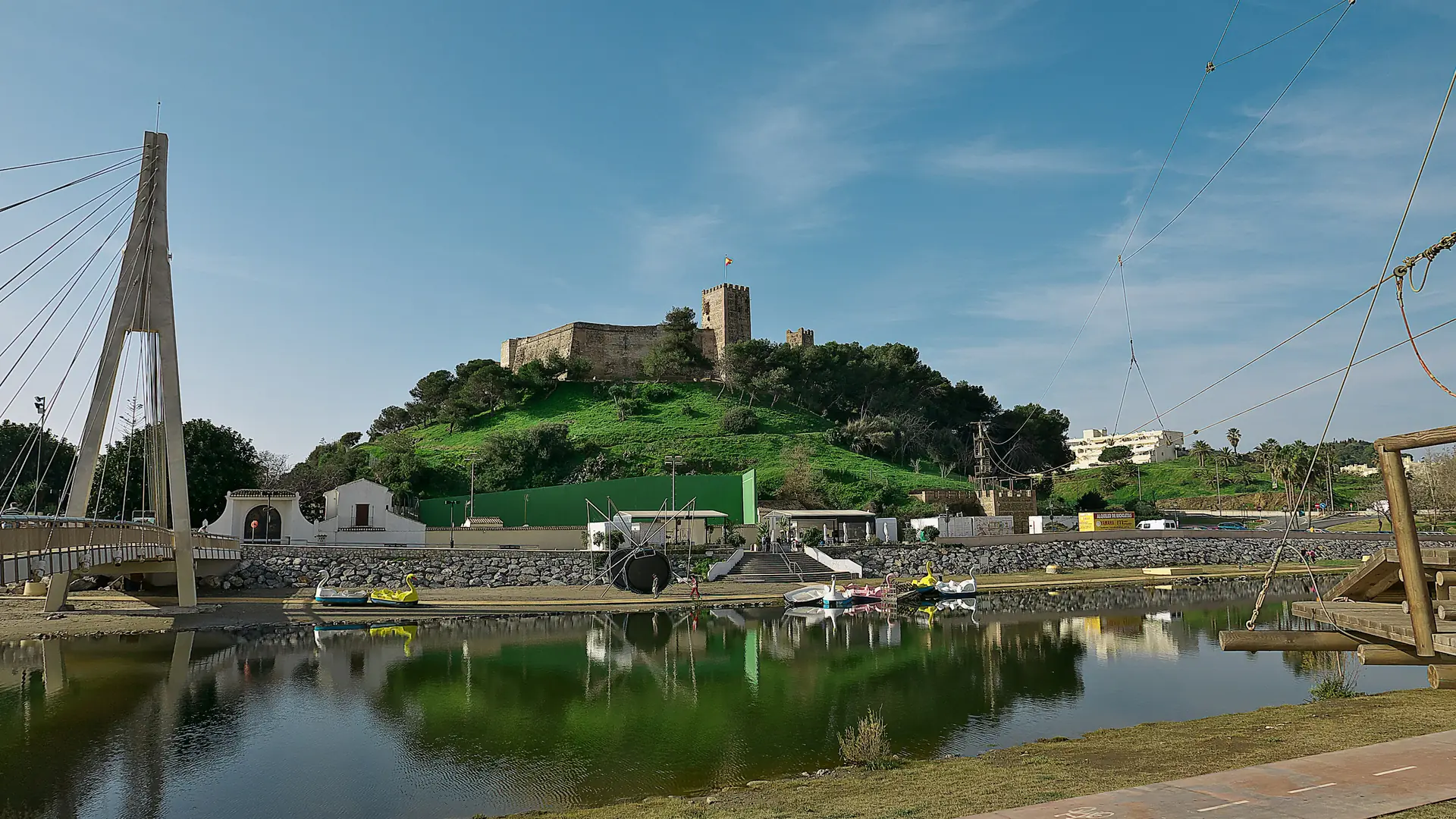 Castillo Sohail on its green hill above Fuengirola, with the river footbridge and boating pond in front