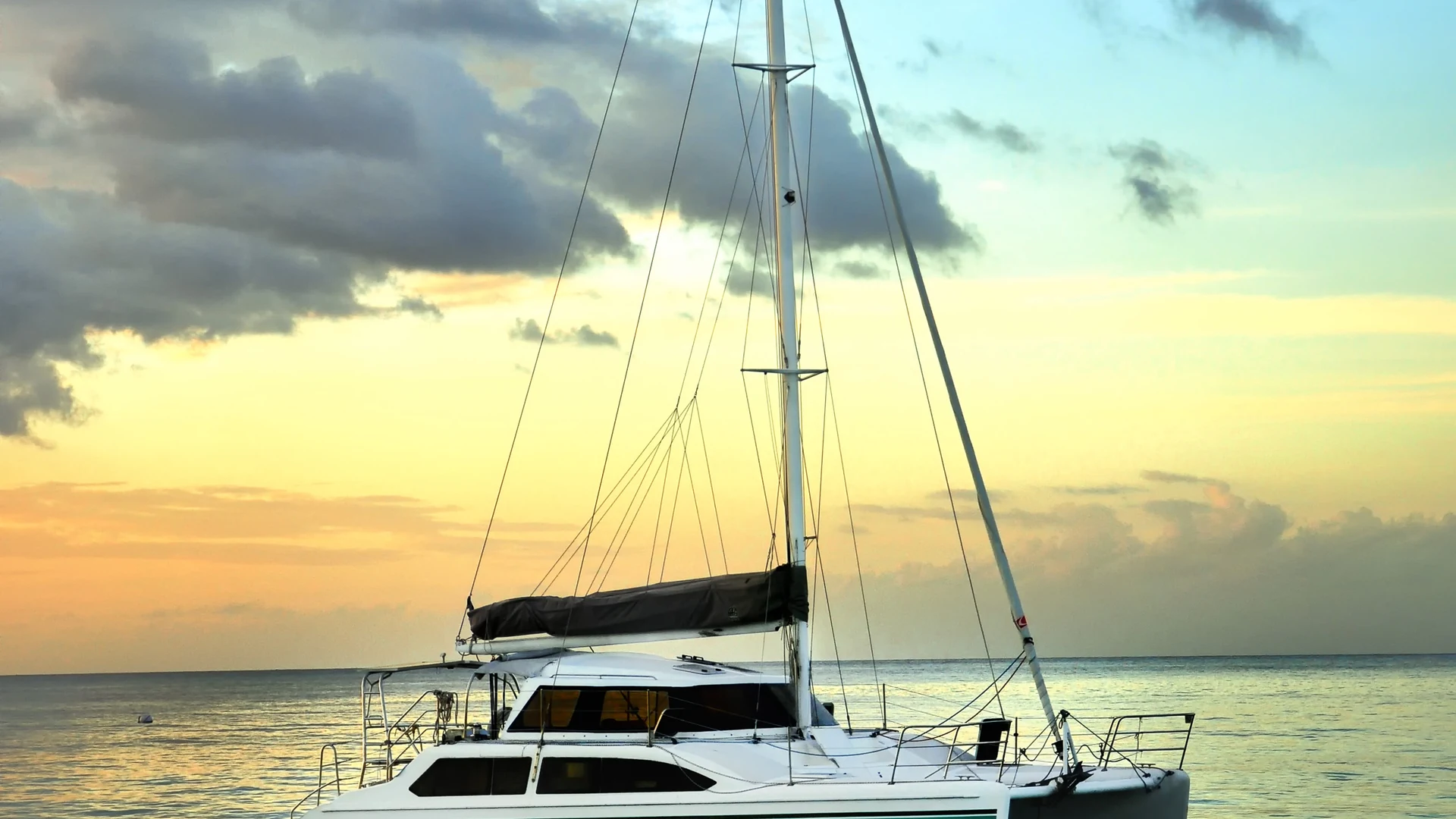 A white luxury catamaran sailing on calm turquoise water at sunset with mountains in the background