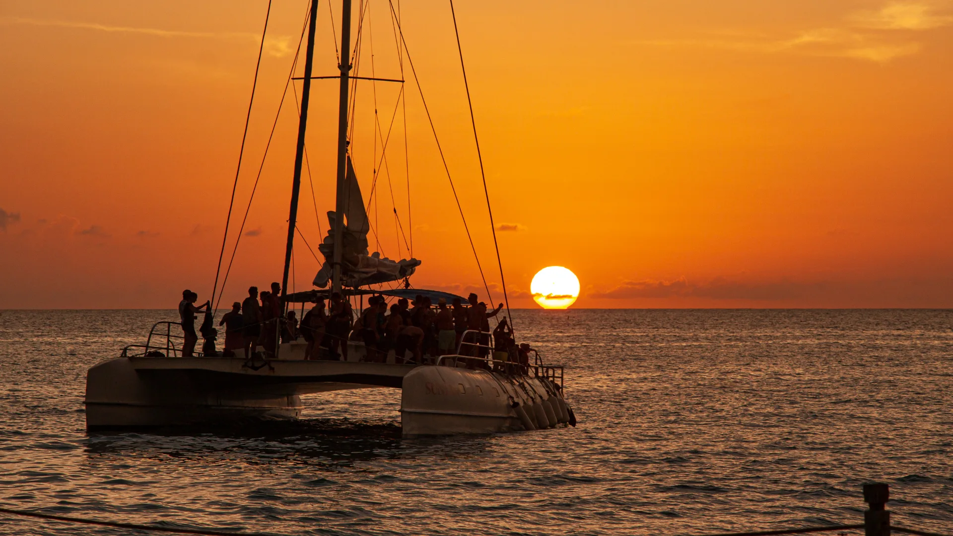Silhouette of a catamaran packed with passengers sailing into a vivid orange sunset off the Málaga coast
