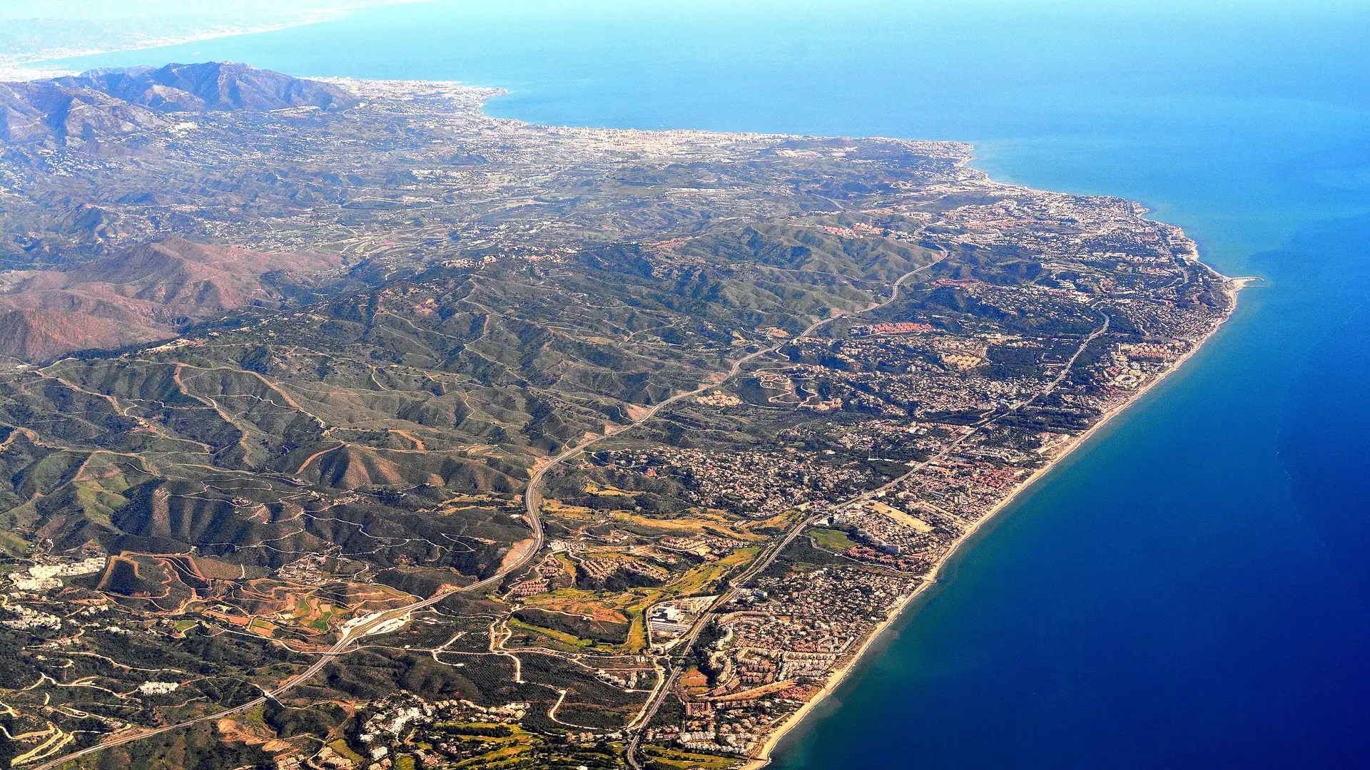 Aerial view of the AP-7 motorway winding along the Costa del Sol coastline between the mountains and the Mediterranean