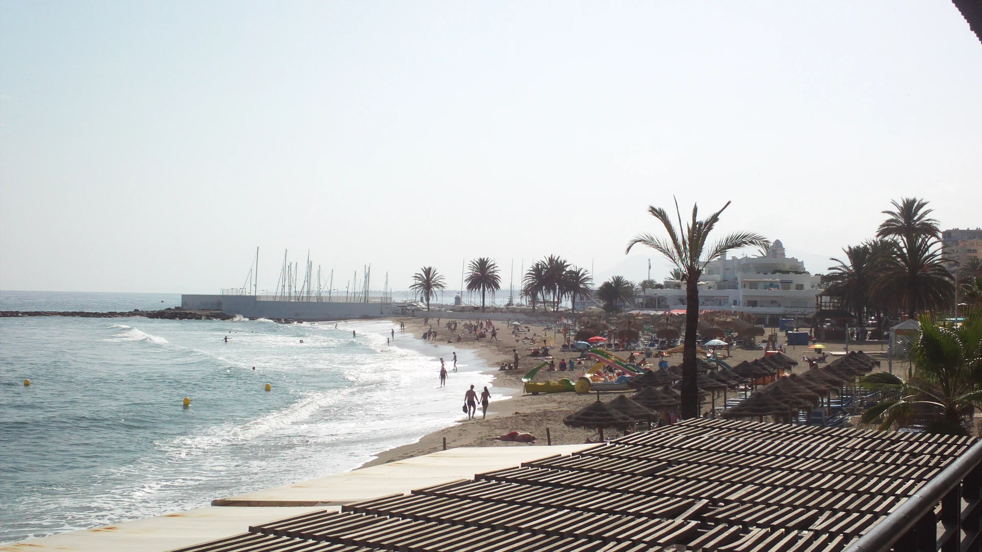 Busy sandy beach in Marbella with straw parasols and families on a sunny day