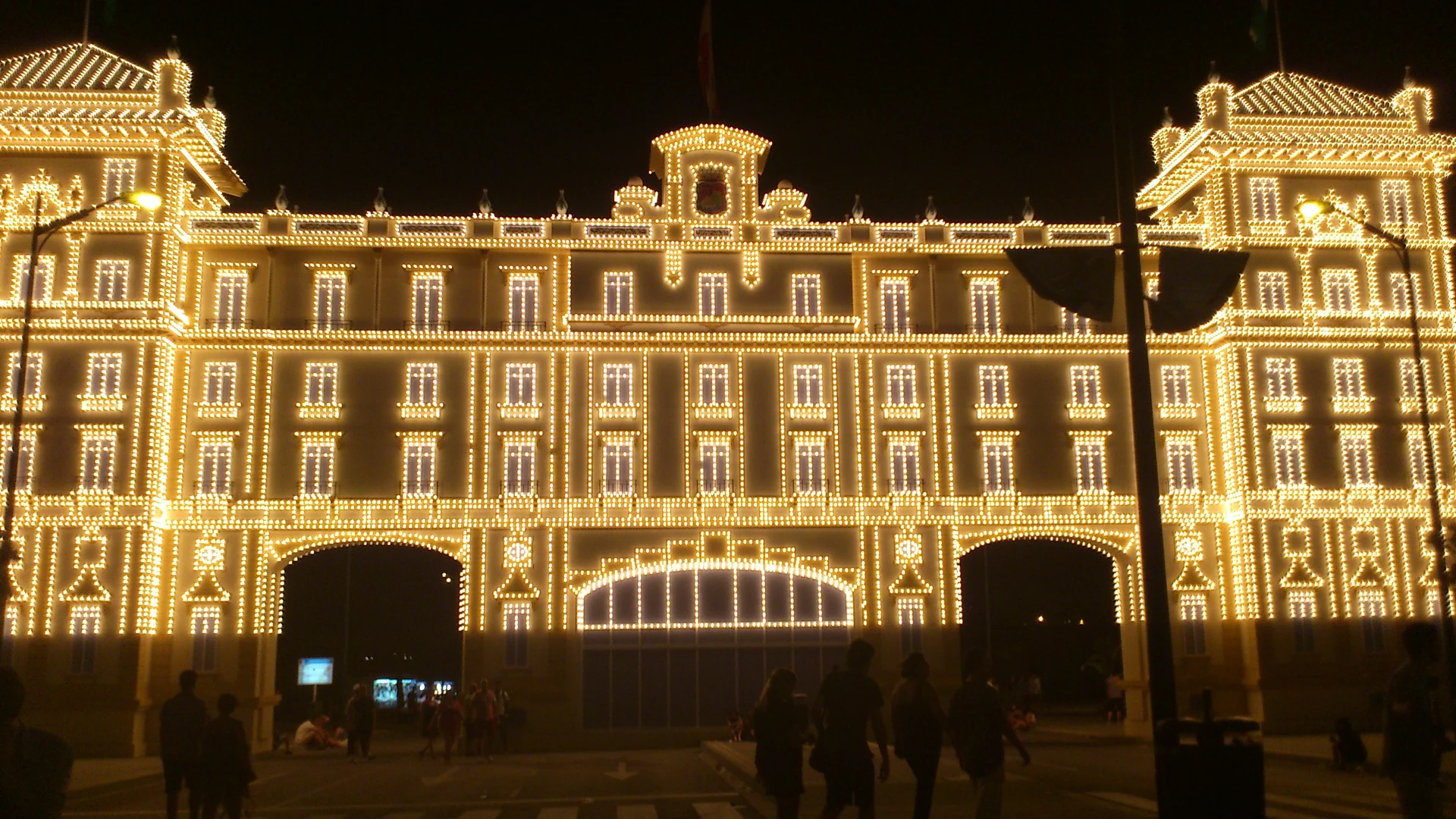 The illuminated entrance gate (portada) of the Feria de Málaga at night