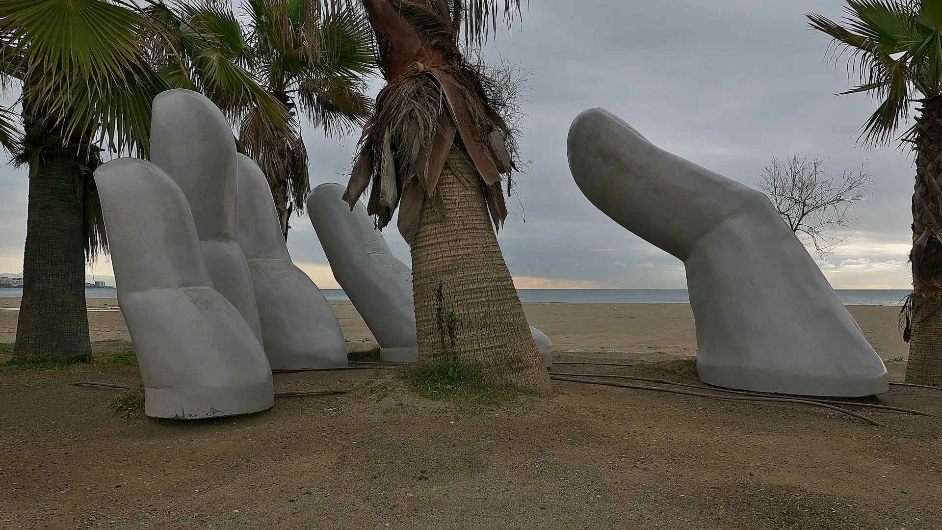 The 'Mano abierta' open-hand sculptures among palm trees on Fuengirola beach