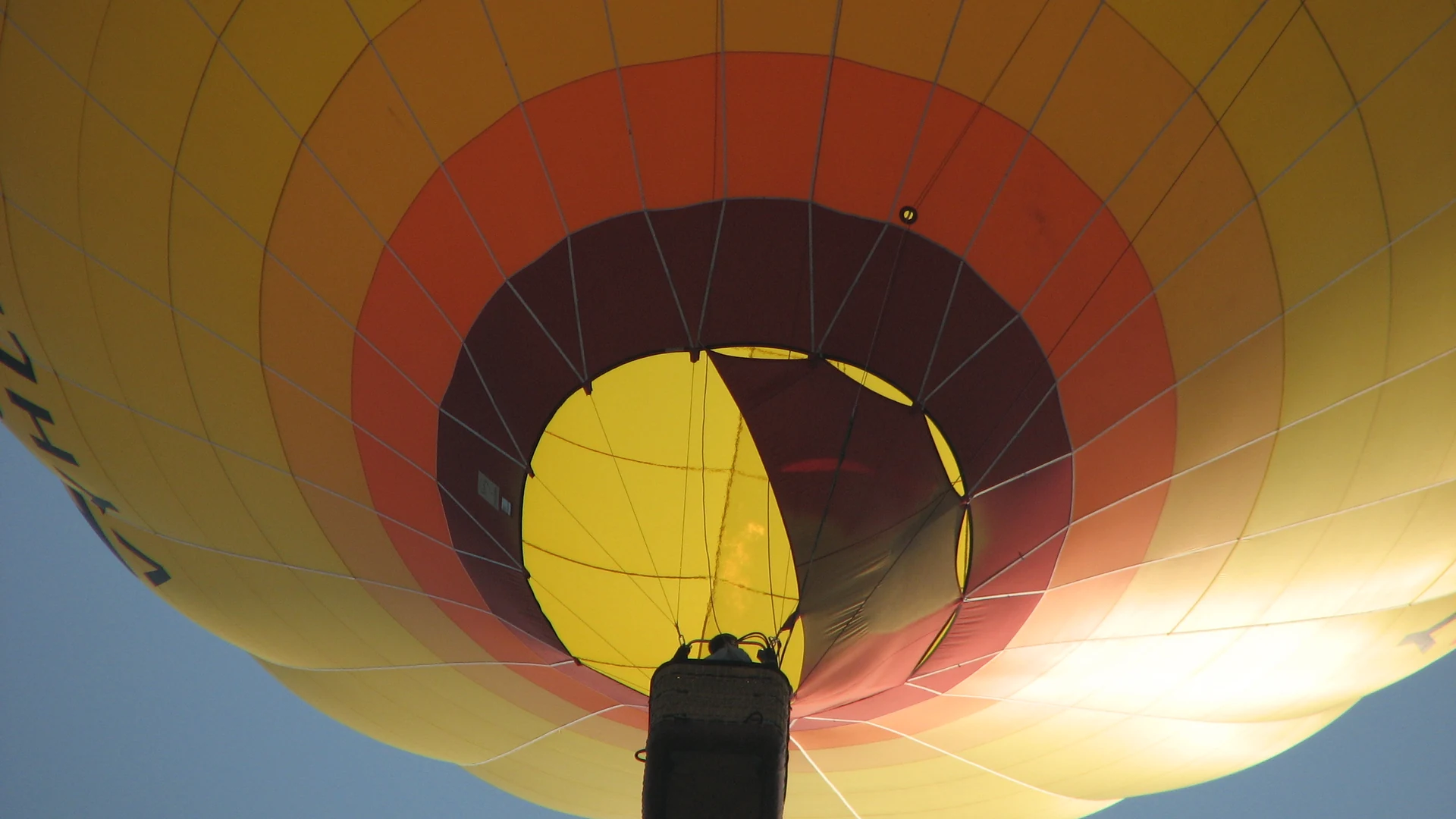 A colourful hot air balloon drifting above open countryside at dawn with blue sky above