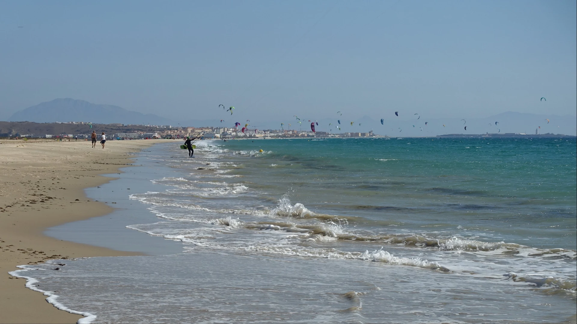 A kitesurfer riding waves at Tarifa beach with the kite high against a blue sky