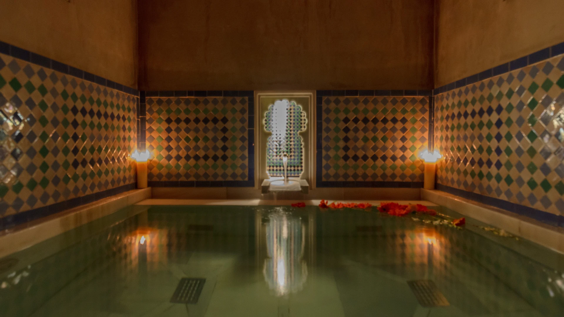 Moorish-tiled thermal pool inside an Andalusian hammam, lit by candlelight