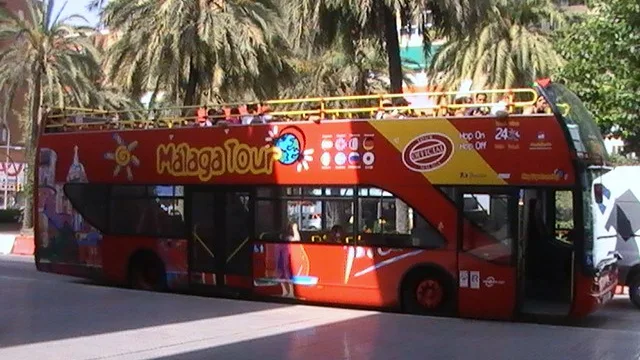 Open-top red City Sightseeing double-decker bus branded "Málaga Tour" parked under palm trees
