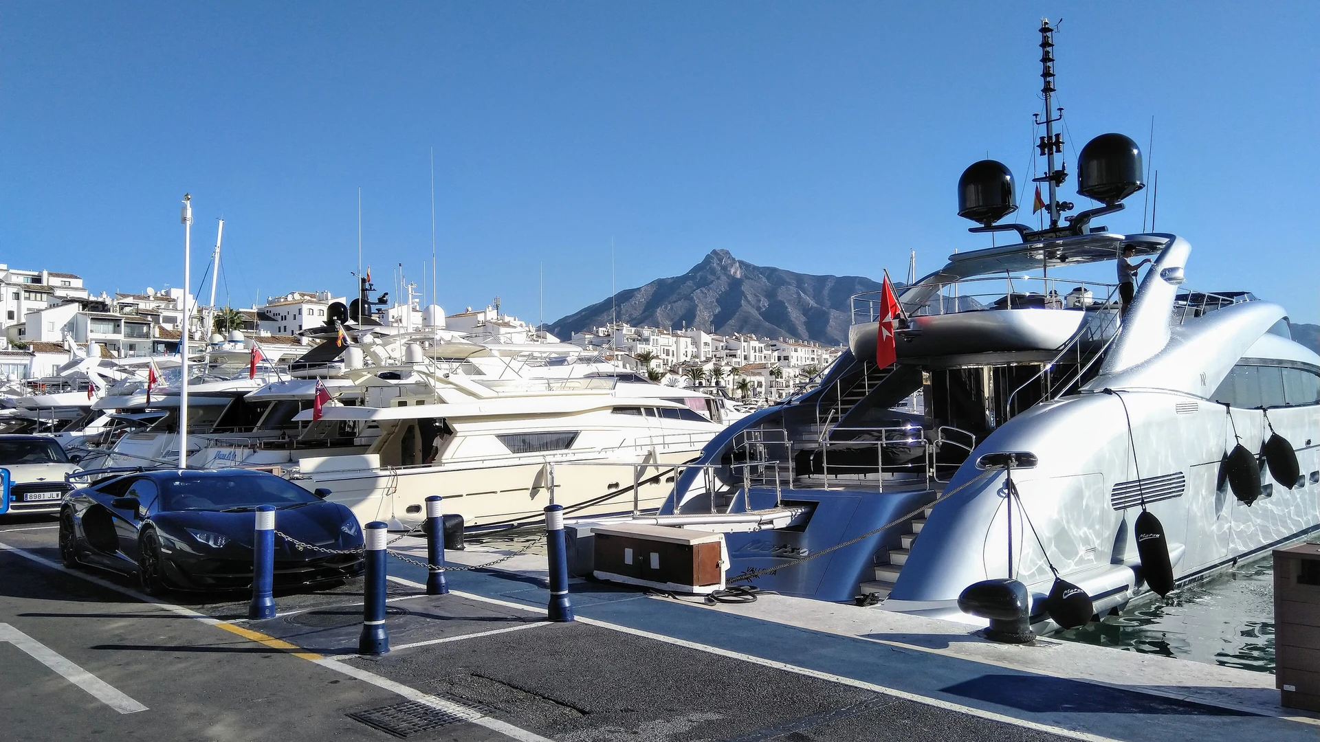 A superyacht and a Lamborghini at Puerto Banús, Marbella, with La Concha mountain behind