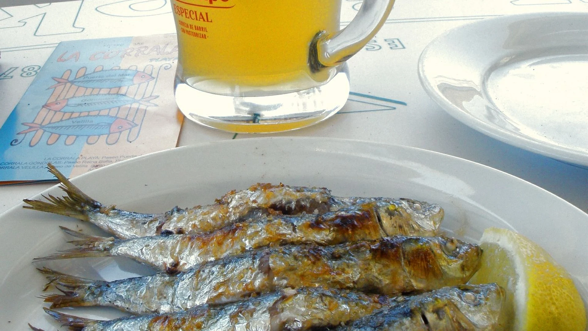A plate of grilled espeto sardines with lemon and a cold beer at a Malaga chiringuito