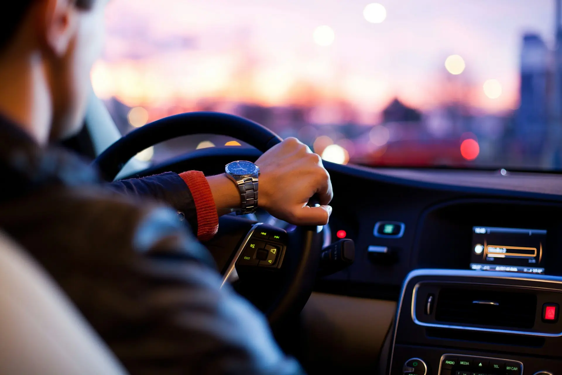 Driver holding a steering wheel at dusk, view from inside the car with blurred city lights