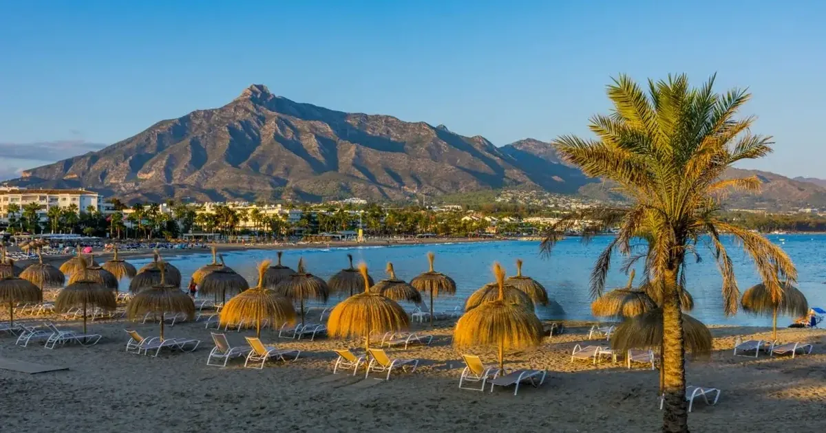Beautiful Marbella beach with golden umbrellas, sun loungers, palm trees and stunning La Concha mountain backdrop on Costa del Sol
