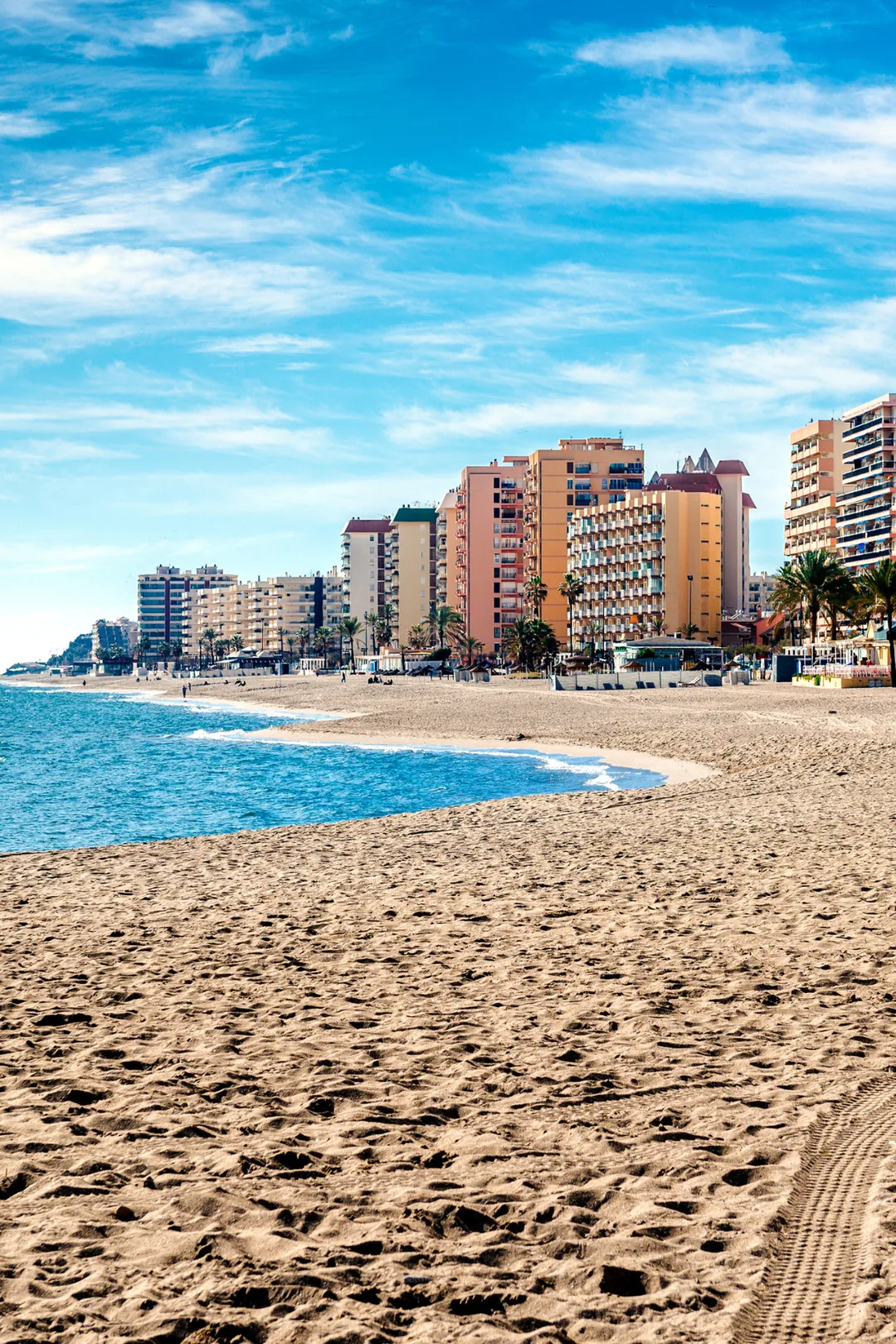 Wide sandy beach in Fuengirola with calm blue sea and a row of hotels and apartment buildings along the seafront