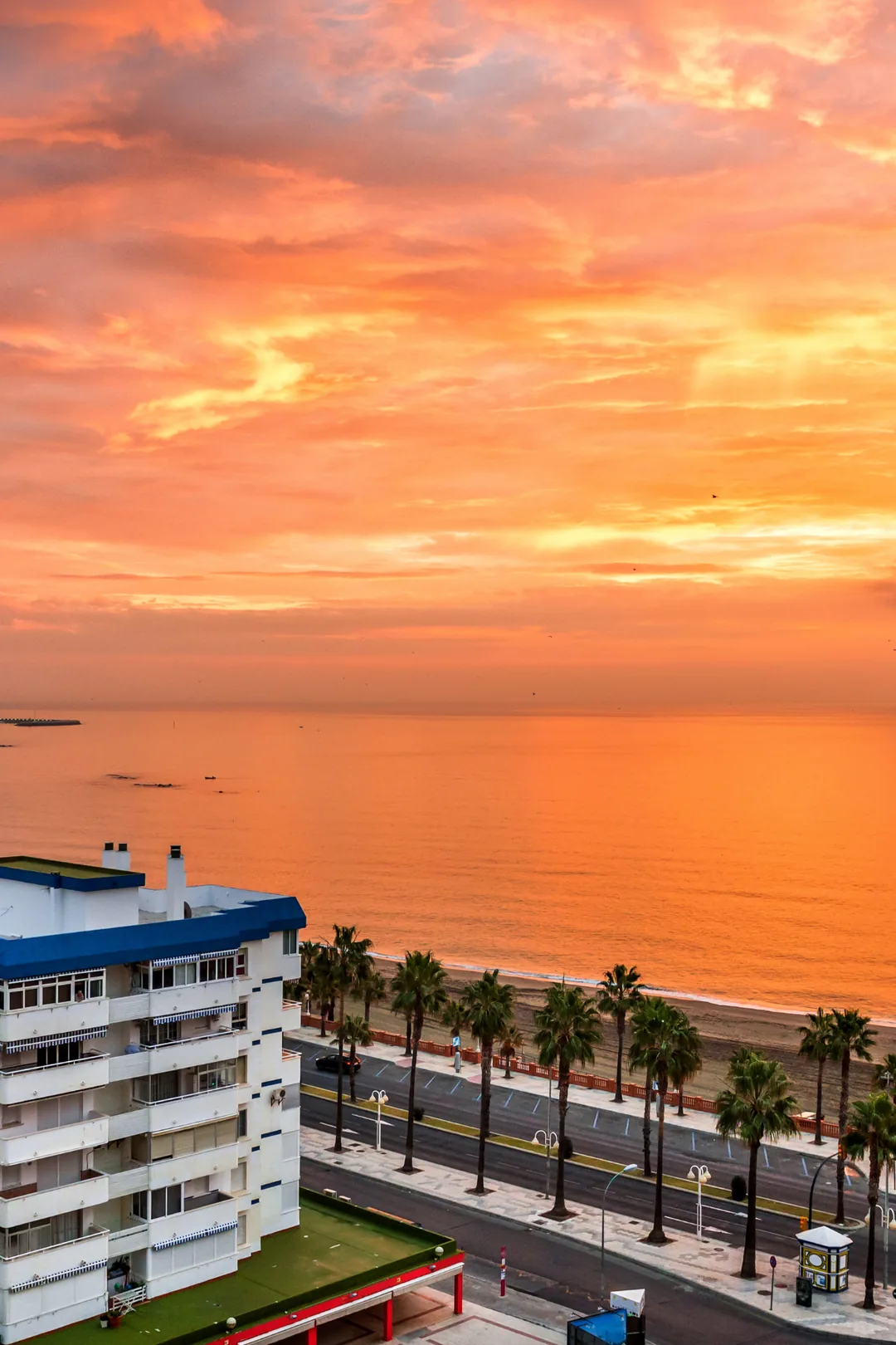 Sunset over the sea in benalmadena with palm-lined promenade and apartment buildings.
