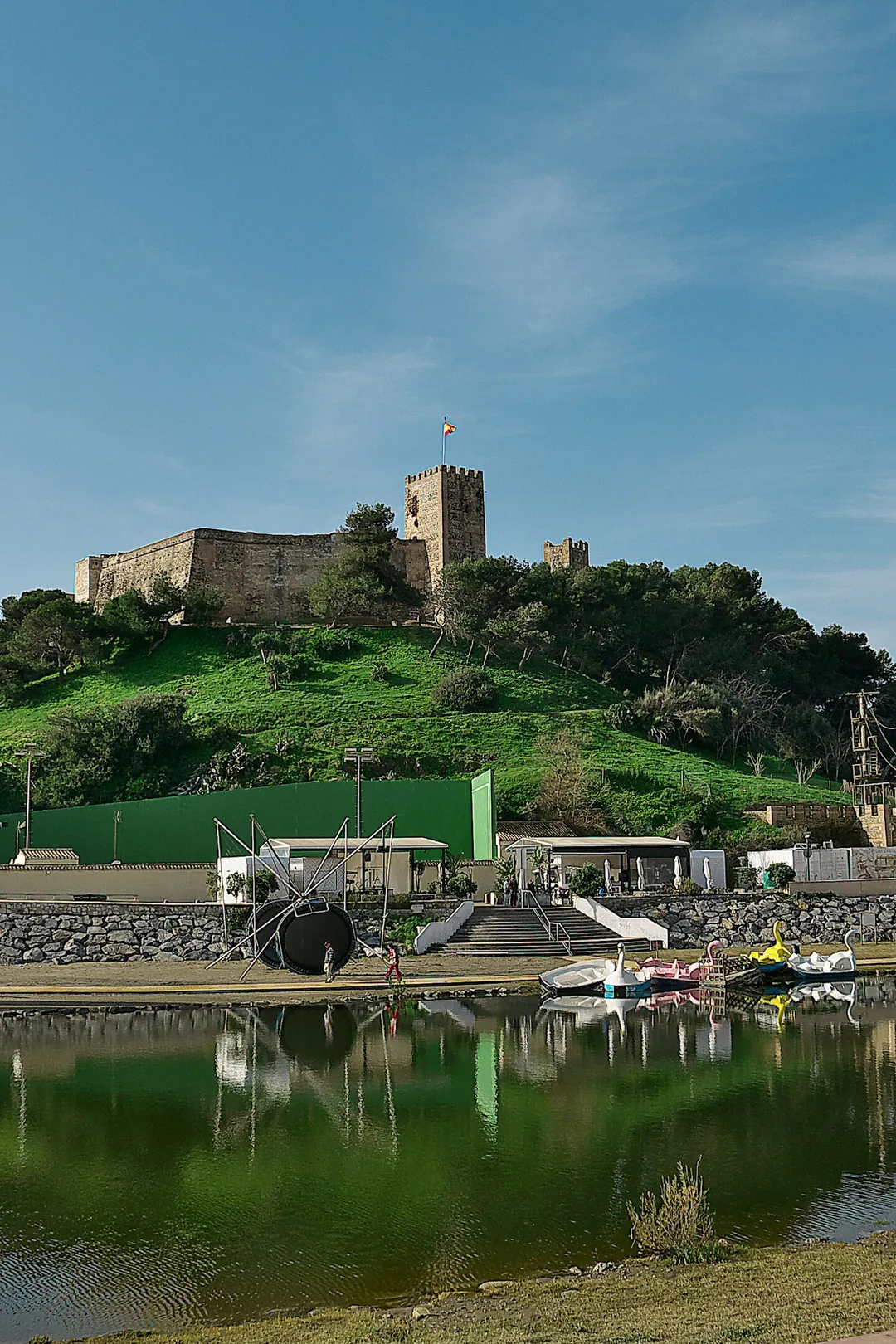 Castillo Sohail on its green hill above Fuengirola, with the river footbridge and boating pond in front