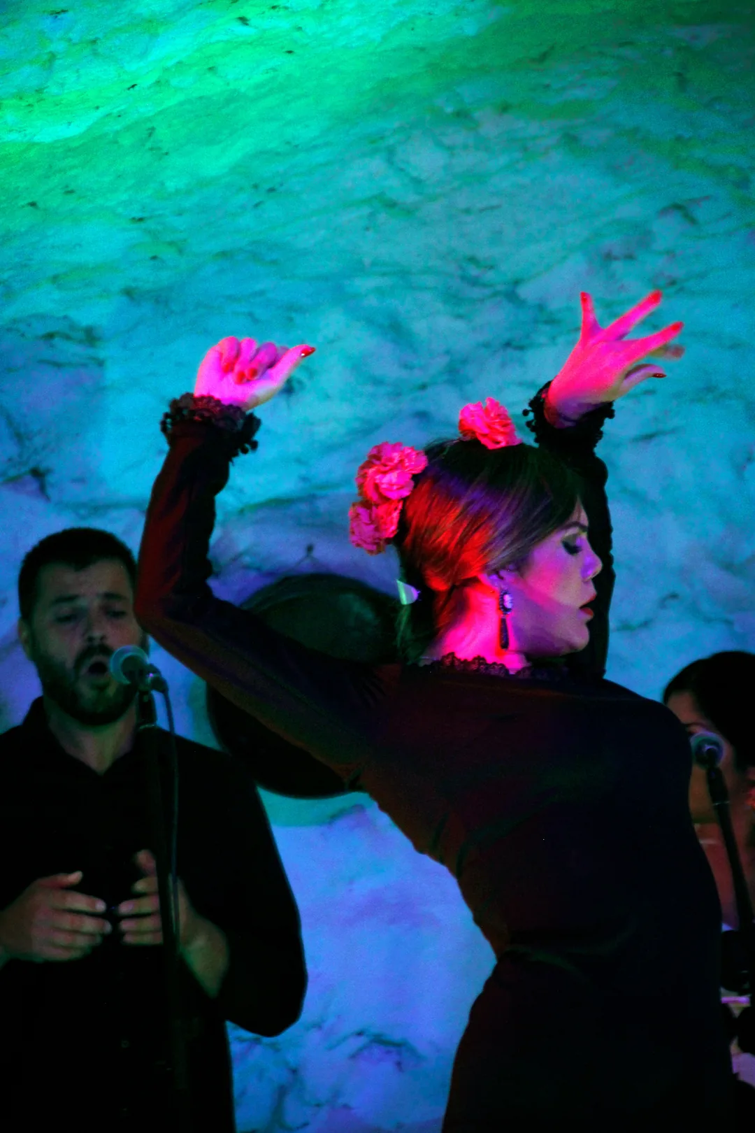 Flamenco dancer with red flowers in her hair performing with a singer at a tablao