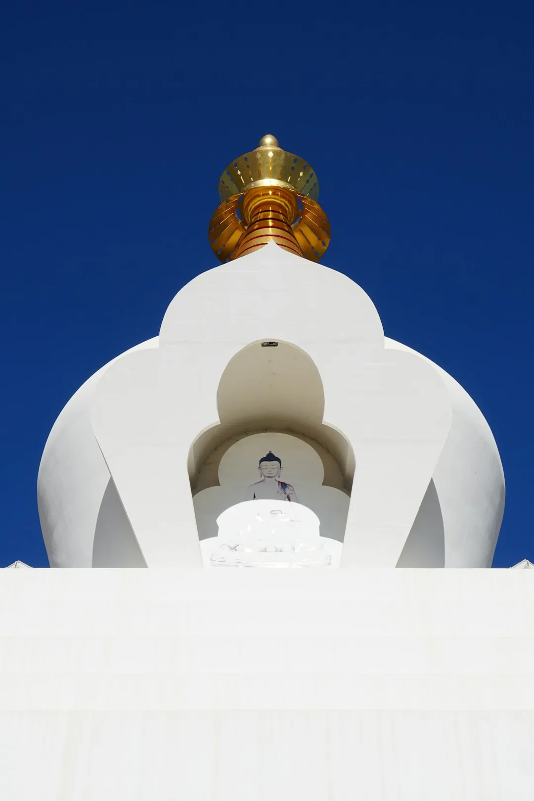 White Buddhist in Benalmádena stupa with a golden spire against a clear blue sky