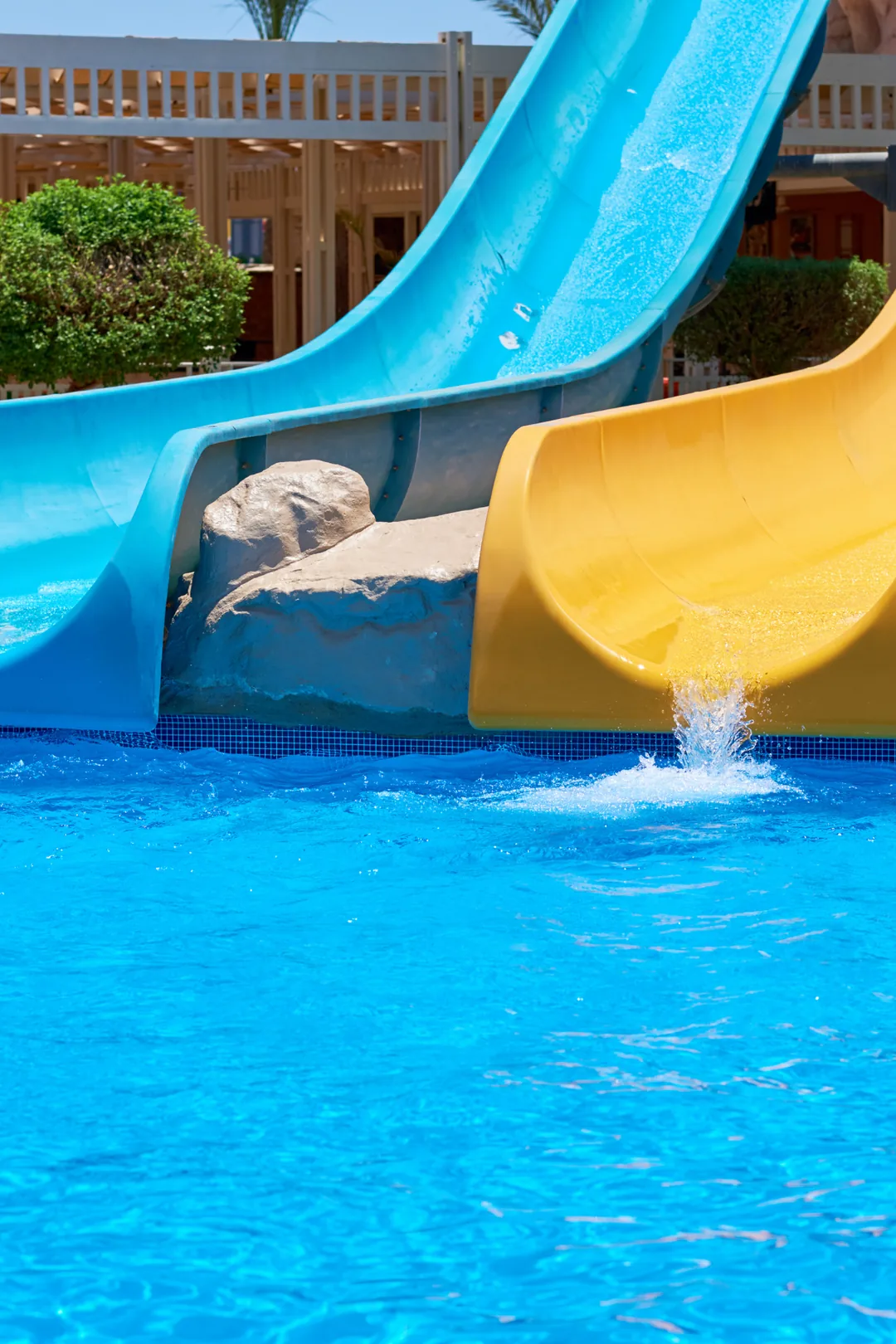 Blue and yellow water slides splashing into a bright pool at a family water park, perfect for kids on holiday