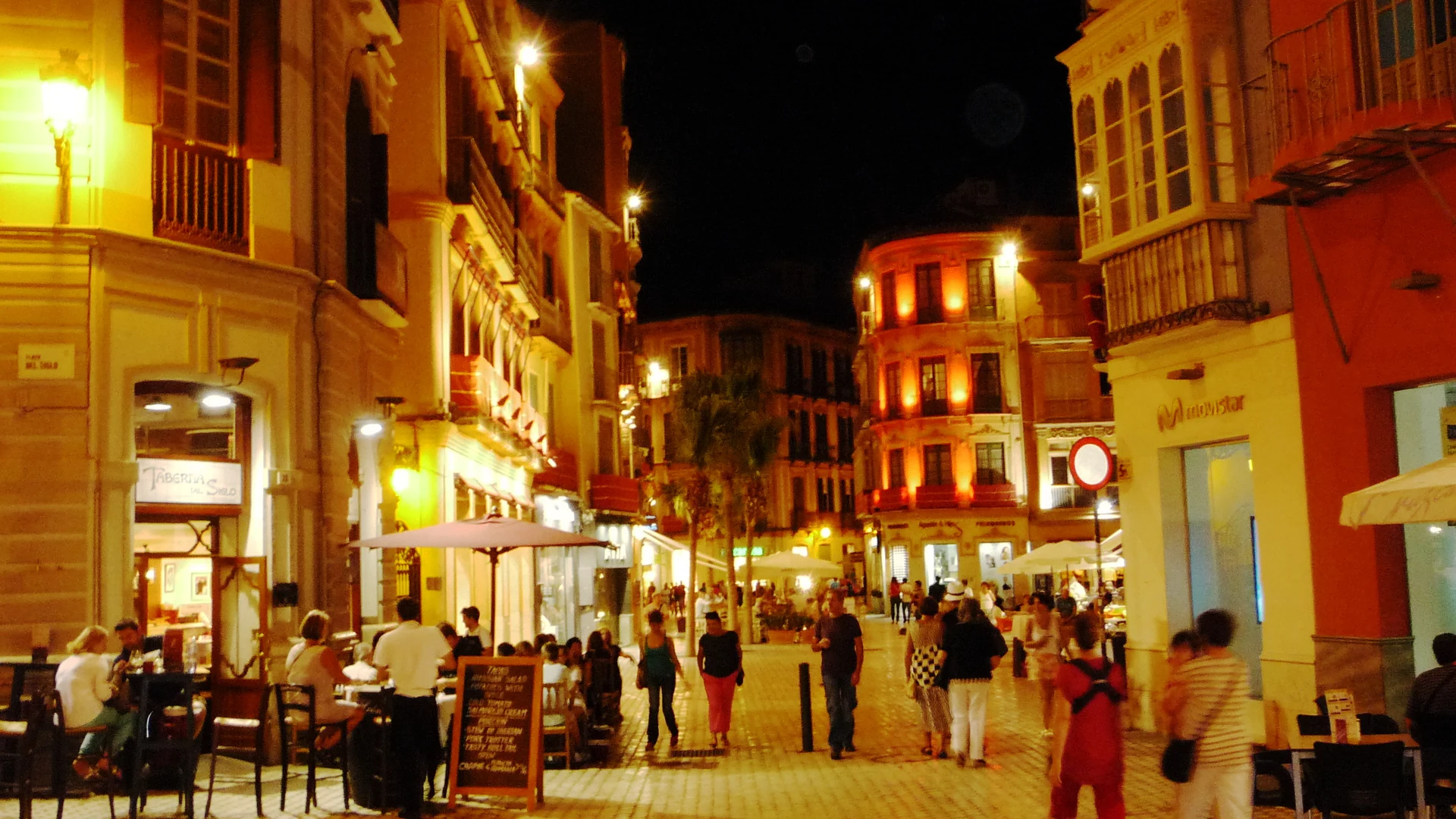A lit square in Malaga's old town at night, lined with bars and terraces