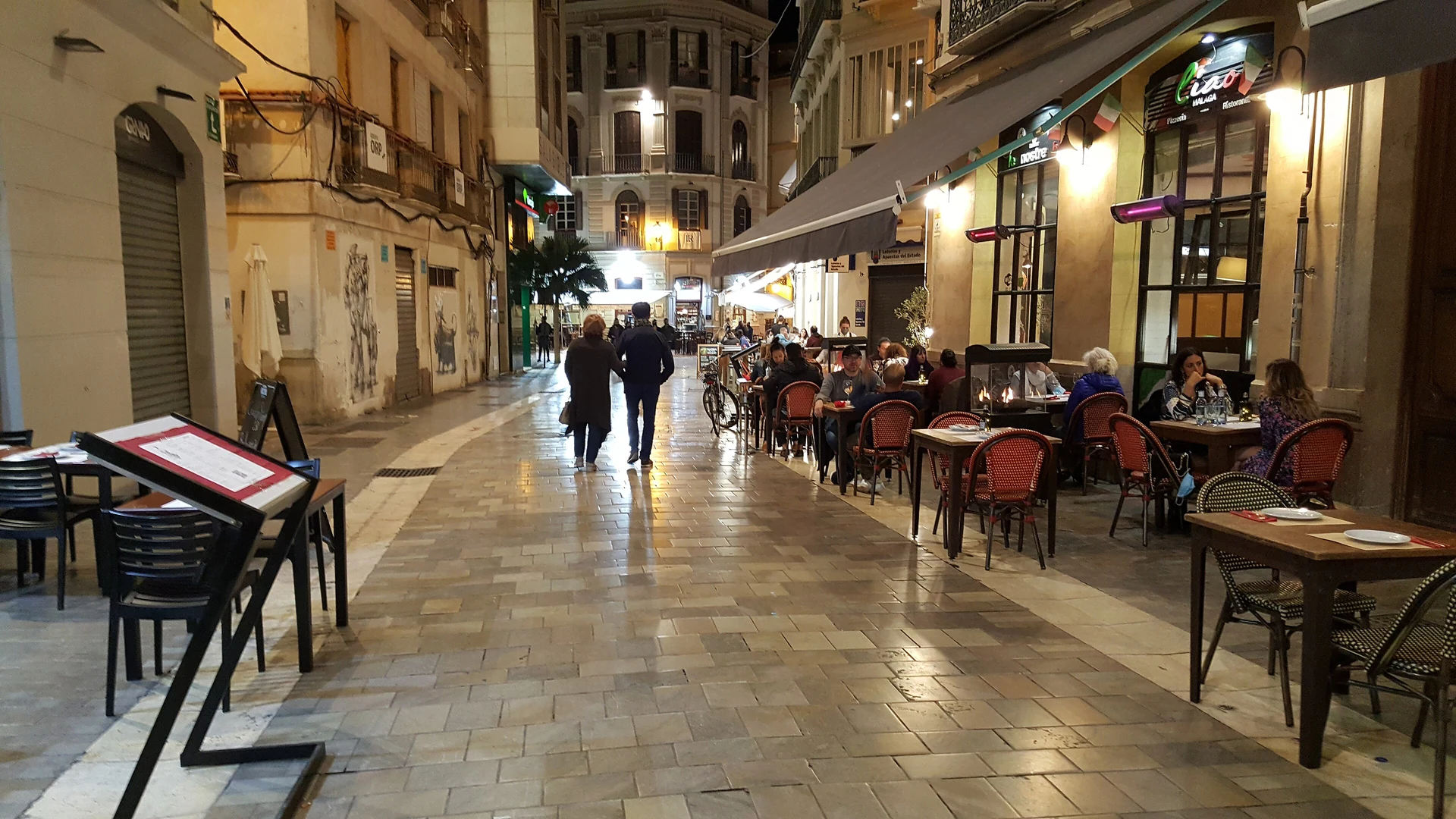 Café terraces on a cobbled stretch of Calle Granada in Malaga's old town at dusk