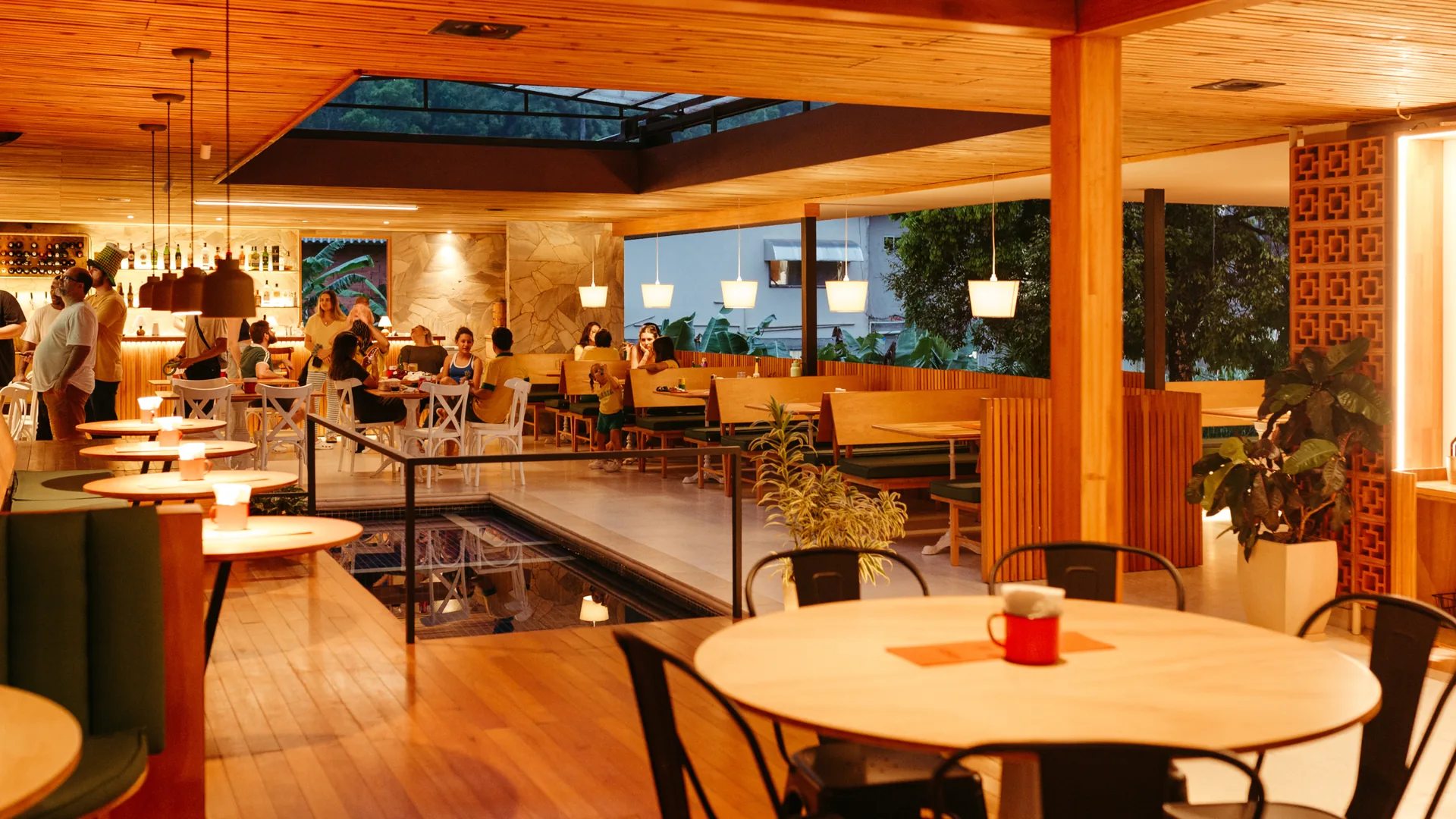 Stylish open-plan restaurant interior with warm wooden decor, pendant lights and guests dining in the evening
