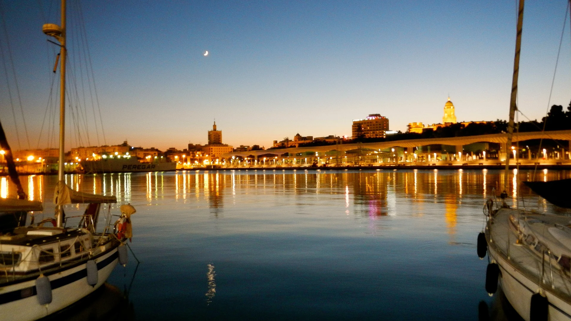Malaga's port at dusk, with yachts and the city lights reflected on the water