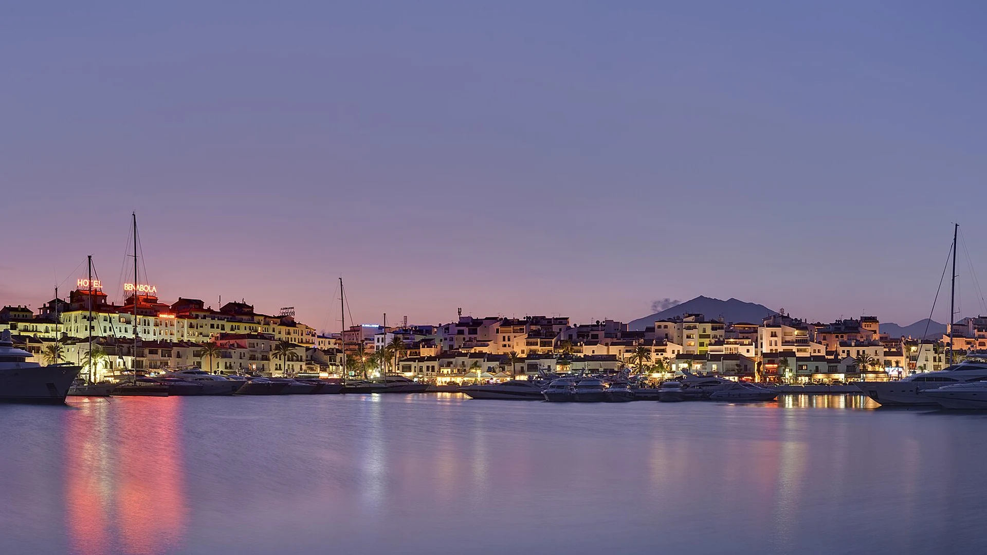 Puerto Banús marina at dusk with the lit waterfront and La Concha mountain behind