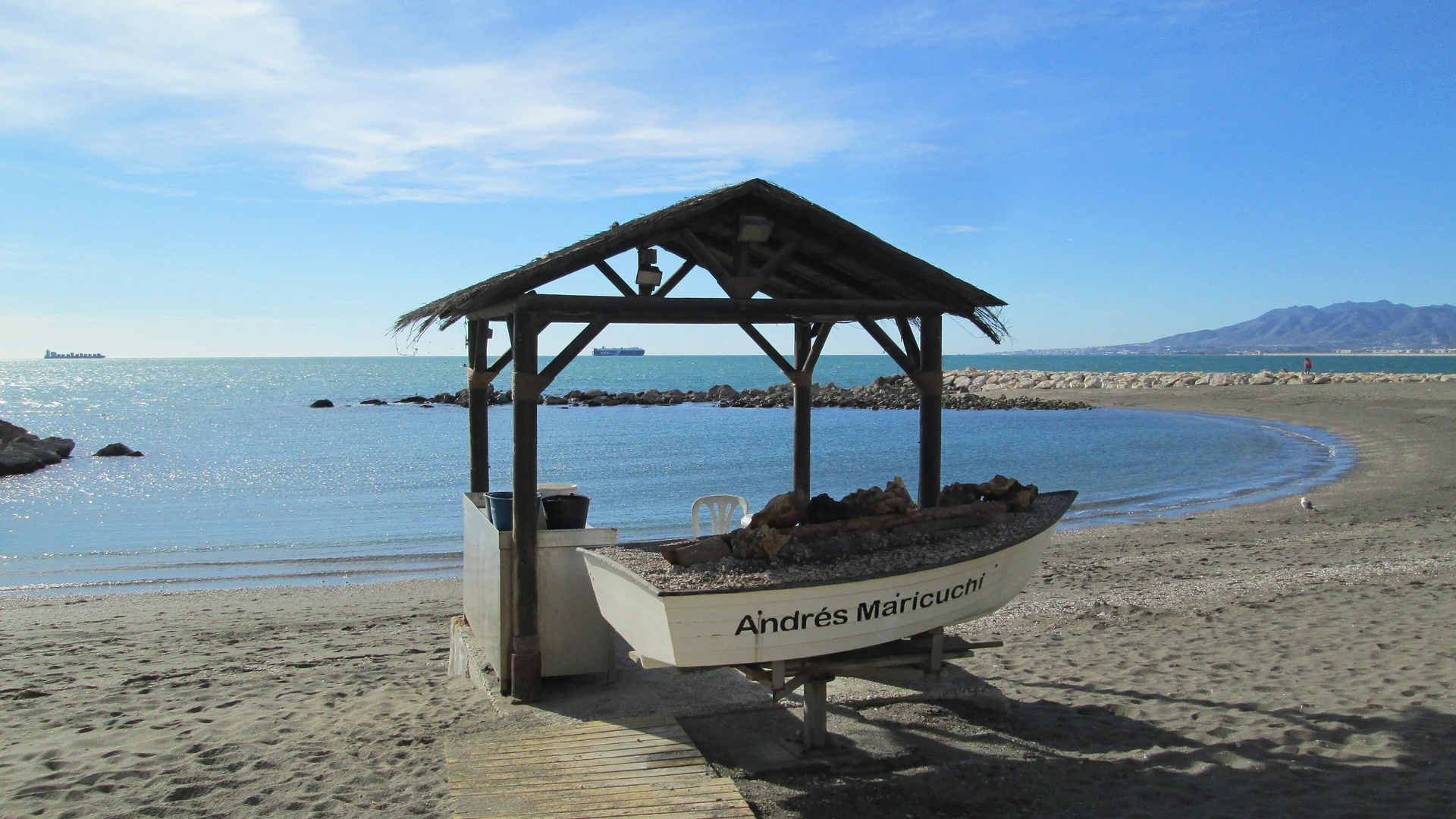 The calm bay at Playa de Pedregalejo in Malaga, with an espeto grilling boat on the sand